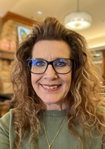 Smiling woman with curly hair and glasses indoors.