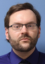 Close-up of a man with glasses and beard against a blue background.