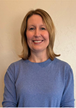 Smiling woman in a blue sweater against a neutral wall.