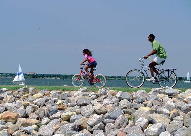 Two people biking along a rocky shoreline with the ocean in the background.