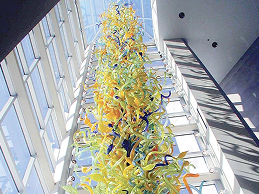 Colorful glass sculpture hanging in a tall, bright atrium.