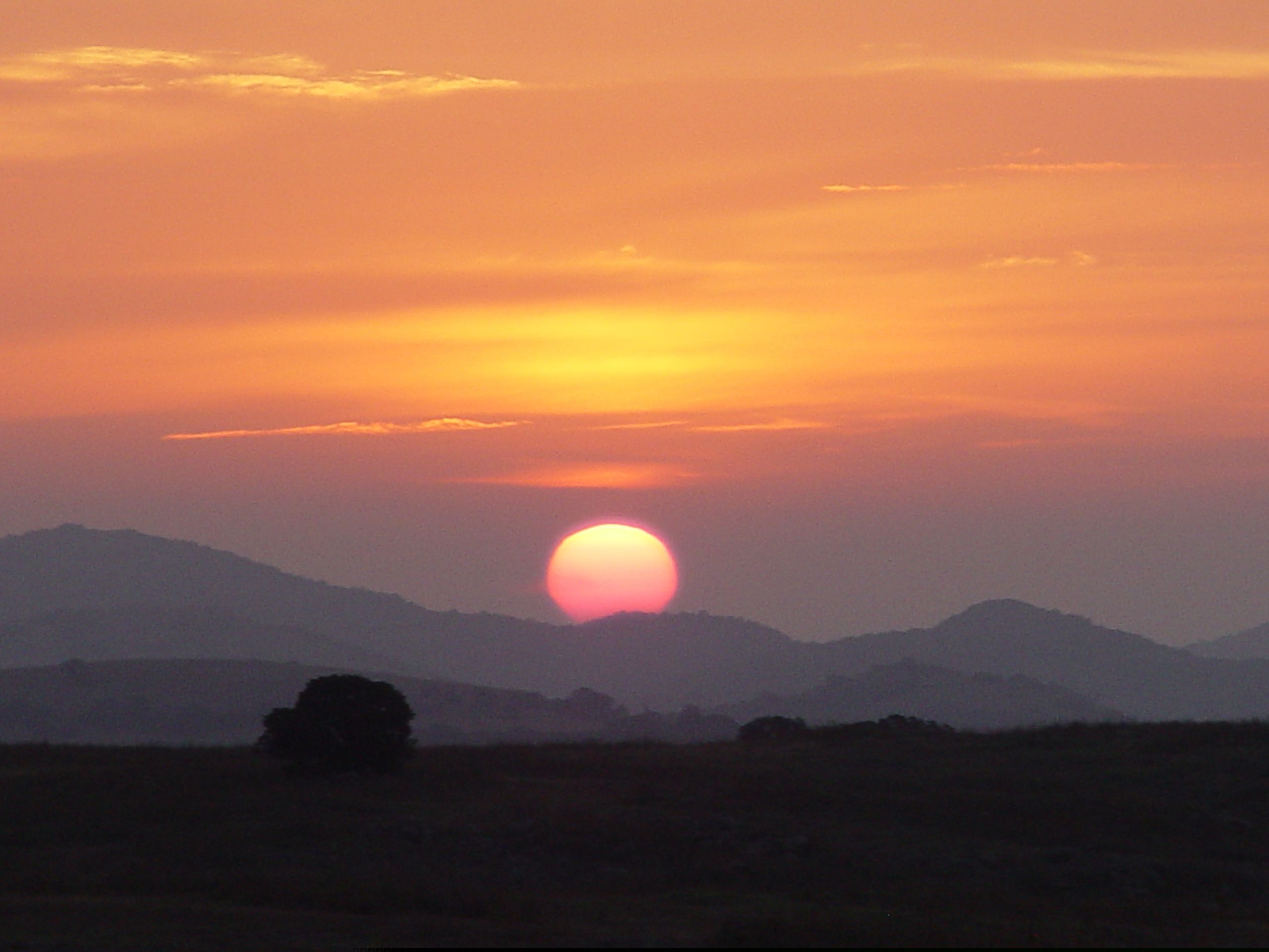 Sun setting behind distant hills with orange sky.